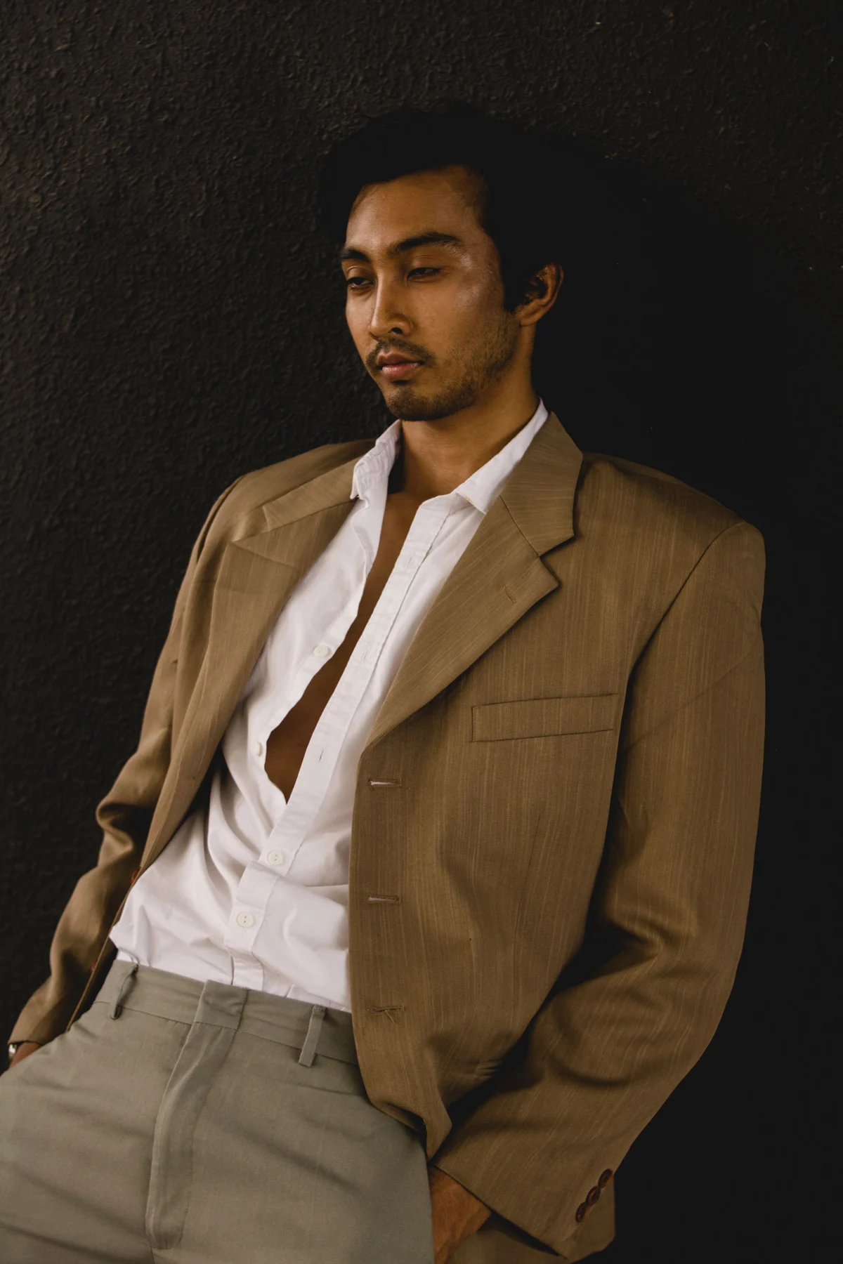 A man in a tobacco-brown blazer, open white shirt and taupe-grey trousers