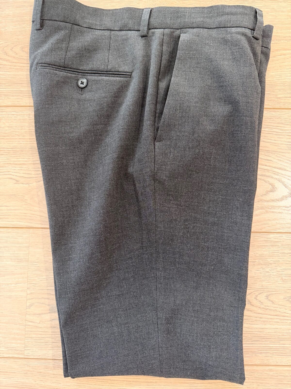 H&M charcoal tailored trousers owned and worn by QWD, photographed flat on a timber floor