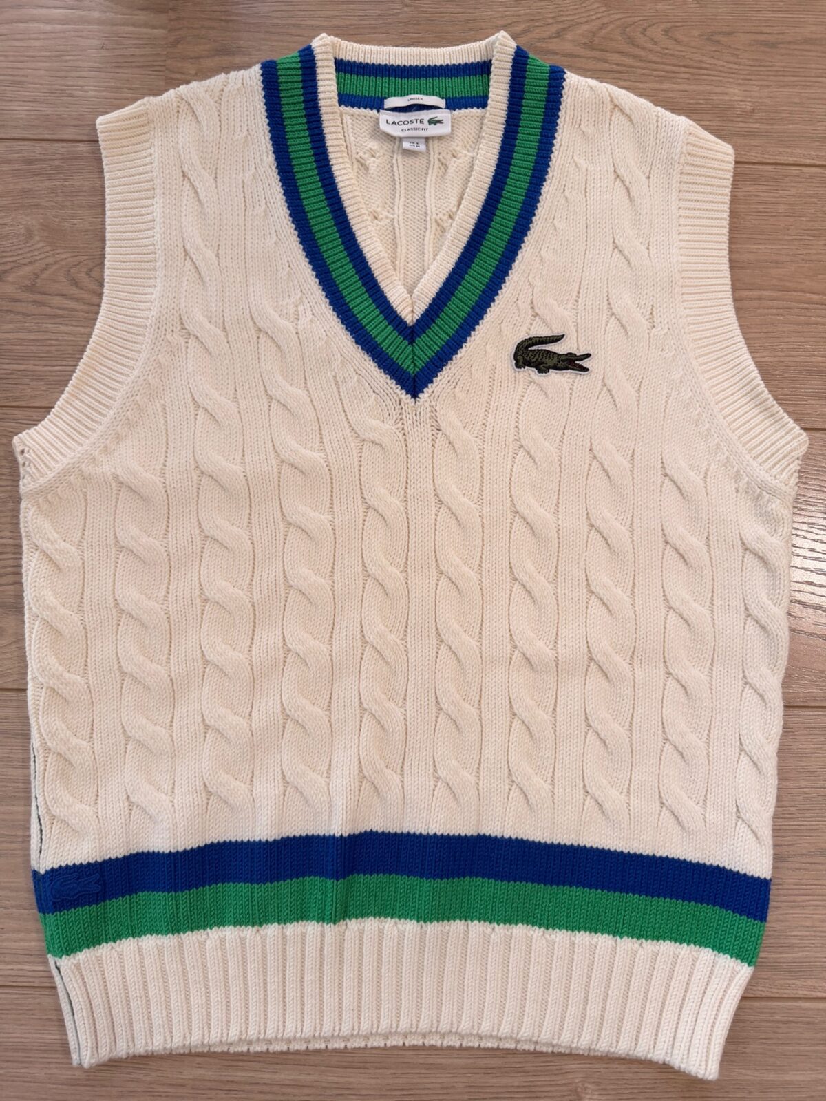 Lacoste cream cable-knit sweater vest with green and navy V-neck trim, photographed flat by QWD